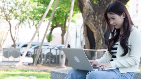 Asian University Student Using Laptop Outdoors in a Sunny Bangkok Park Stock Footage 336845334