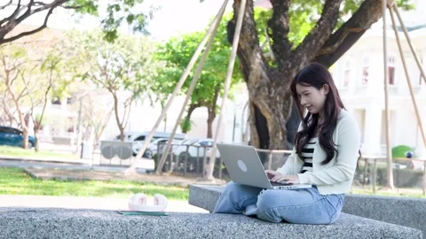 Asian University Student Using Laptop While Sitting Outdoors in a Park Stock Footage 337600459