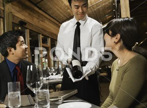 Asian waiter showing wine to couple Stock Photos