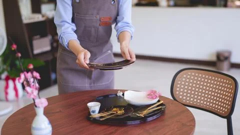 Asian waitress serving customer table setting wooden round table at modern .. Stock Photos