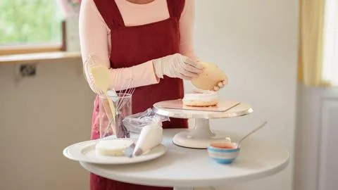 Asian woman assembling cake layer on pedestal stand while baking homemade d.. Stock Photos