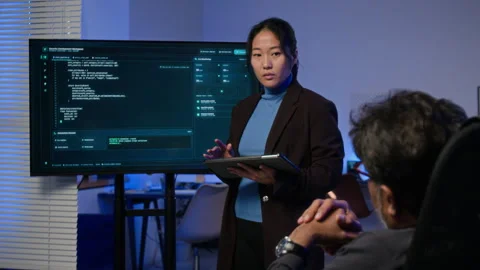 Asian Woman Discussing Cybersecurity Code with Colleague 動画素材 347310387