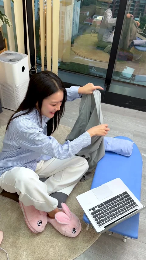 Asian Woman Folding Laundry While Working on Laptop at Home Stock Footage 346676019