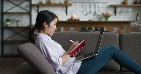 Asian woman learning distantly using laptop computer and writes notes while Stock Footage 196940405