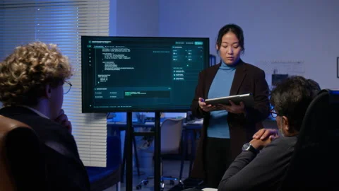 Asian Woman Presenting Cybersecurity Code on Monitor to Colleagues Stock Footage 347291725