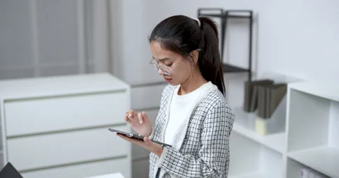 Asian woman reading documents while standing at desk during business task in 库存影片 336377532