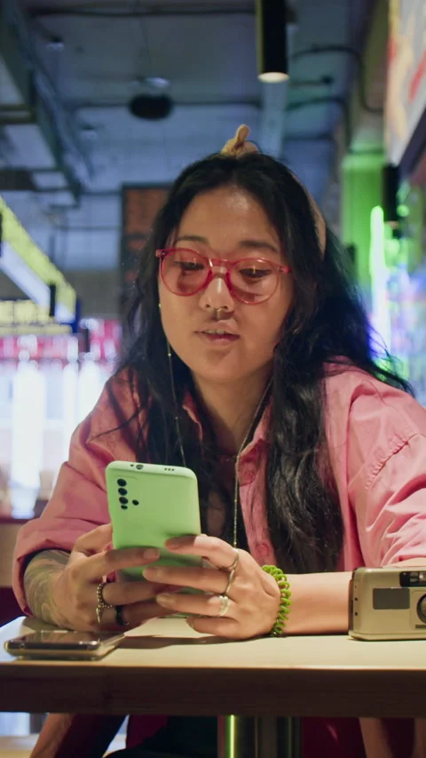 Asian Woman Sitting in Cafe Using Mobile Phone While Looking Around Stock Footage 343878148