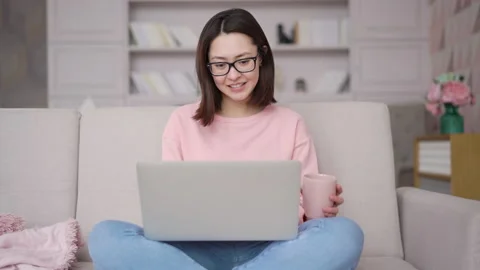Asian woman sitting on sofa using laptop computer looking at screen typing Stock Footage 152723622