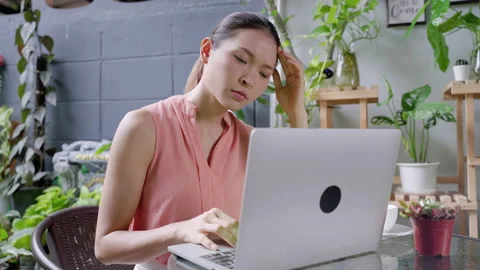 Asian woman stressed in front of her laptop in the garden while working Stock Footage 166311682