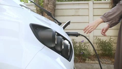 Asian woman unplug the charger from the electric vehicle and walk away Stock Footage