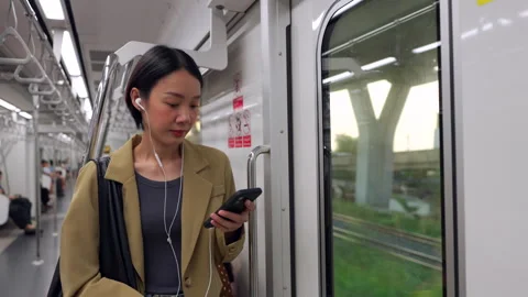 Asian woman using smartphone during morning commute on a city train Stock Footage 345959935