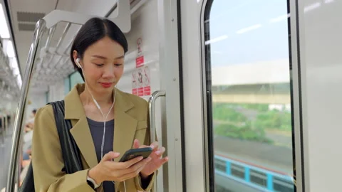 Asian woman using smartphone during morning commute on a city train Stock Footage 345960079