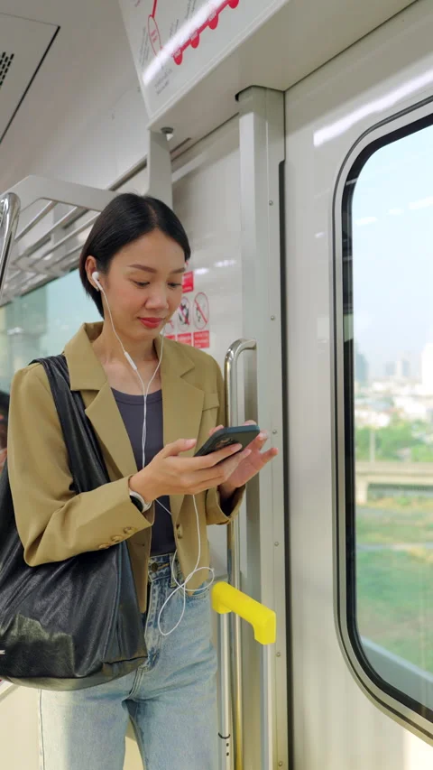 Asian woman using smartphone during morning commute on a city train Stock Footage 345960099