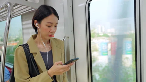 Asian woman using smartphone during morning commute on a city train Stock Footage 345960125