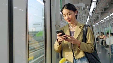 Asian woman using smartphone during morning commute on a city train Stock Footage 345960159
