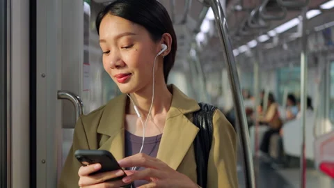 Asian woman using smartphone during morning commute on a city train Stock Footage 345960499