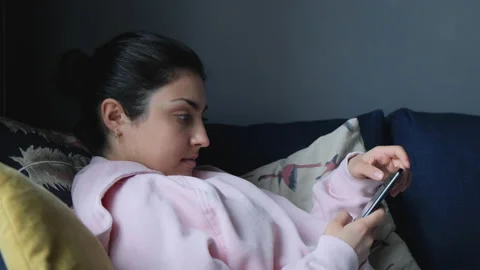 Asian woman using smartphone while lying on home sofa in her living room Video stock 134943540