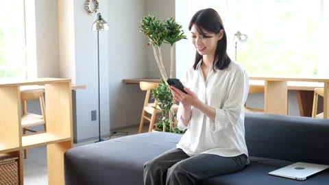 Asian Woman Using Smartphone While Sitting on Sofa in Modern Office Stock Footage 344092132
