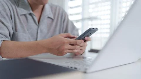 Asian woman using smartphone while working with laptop in bright modern wor.. Stock Photos