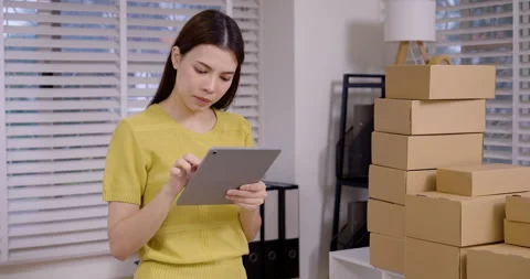 Asian woman using tablet to check e-commerce order, organizing stacked parcel Vídeos de archivo 335143767