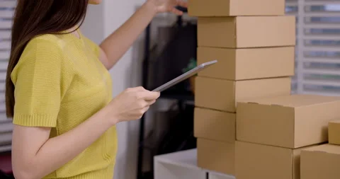 Asian woman using tablet to update e-commerce order, managing stacked parcels Vídeos de archivo 330842234