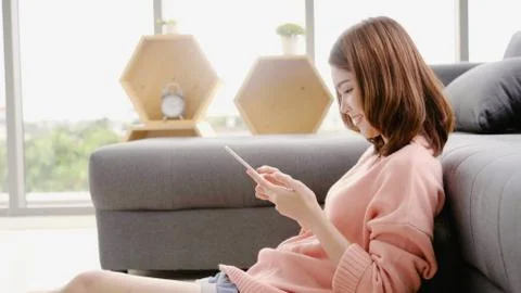 Asian woman using tablet while lying on home sofa in her living room. Stock Photos