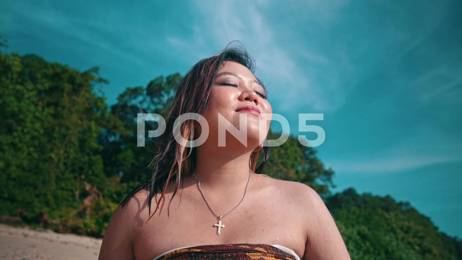 an Asian woman with wet blonde hair is sitting on the beach while enjoying  ..