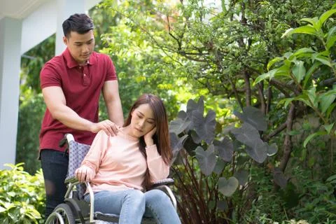 Asian woman on wheelchair and Unhappy and painful. A Man standing behind whee Stock Photos