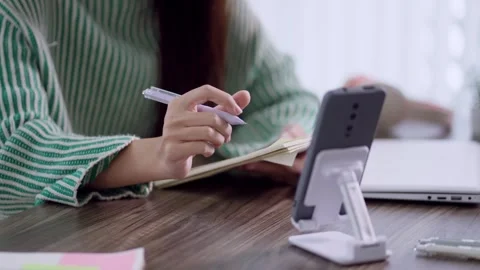 Asian woman writing notes in planner while learning from smartphone on desk.. Stock Footage 342533514