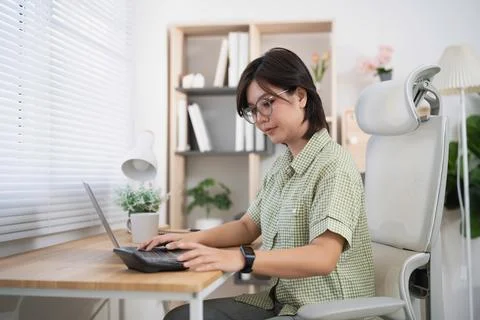 Asian womans hand using calculator with laptop on wooden desk in minimalist.. Stock Photos