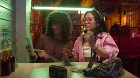 Asian Women Sharing Screen on Mobile Phones in Neon Cafe Stock Footage 343869760