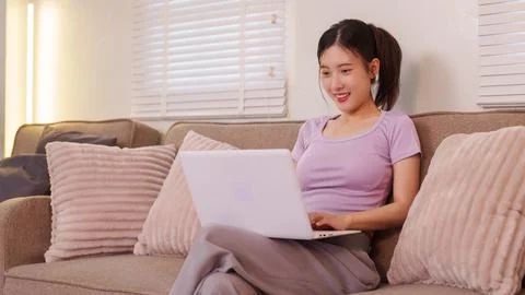 Asian women using laptop computer working from home sitting on sofa couch i.. Stock Photos