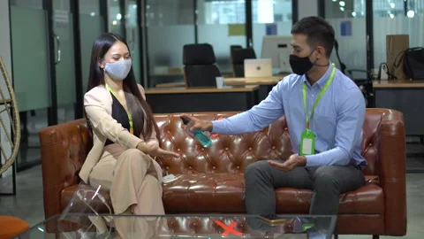 Asian worker in face mask using alcohol spray clean hands meeting on sofa in Stock Footage 140124640