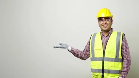 Asian worker in uniform hard hat safety glasses open hands palm up pointing to b Stock Footage 144260227