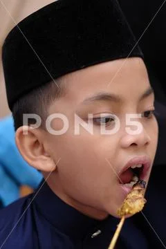 Asian young boy ate Satay while visiting their relatives during Eid al-Fitr Stock Photos