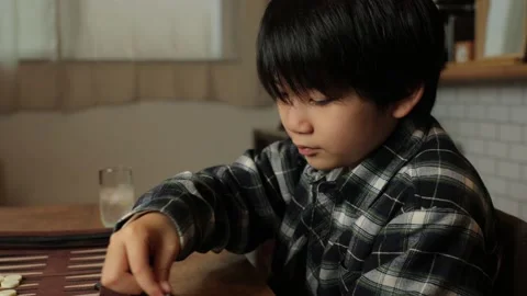 Asian young boy playing backgammon at home. Roll dices. Profile. Stock Footage 224243231