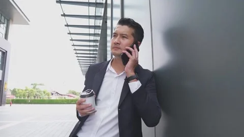 Asian young Businessman Using Mobile Phone and holding coffee cup stand outdoor. Stock Footage 234975155