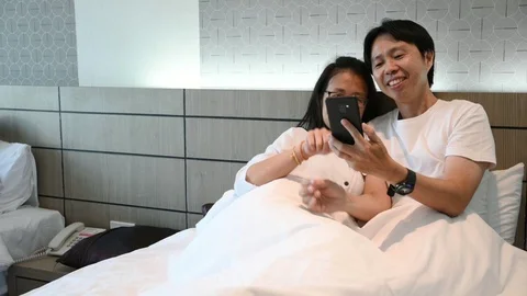 Asian young couple using smartphone lying on bed together Stock Footage 124114642