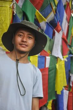 A Asian young guy looking at camera, standing against Buddhist prayer flags Foto stock