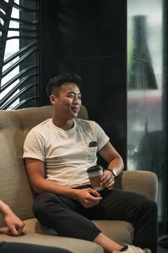 Asian young handsome man sitting in coffee shop, drinking coffee and smiling Stock Photos