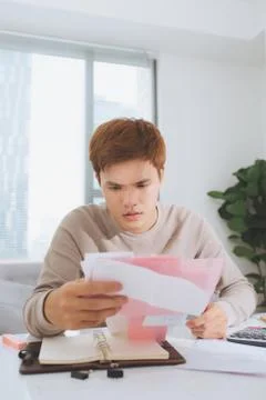 Asian young man counting using calculator and stress in problem with expenses Stock Photos
