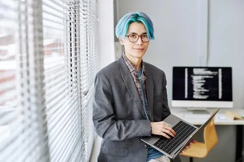 Asian young man looking at camera and holding laptop by window 스톡 사진