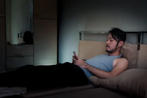 Asian Young man using Mobile Phone on the bed at night.. Stock Photos