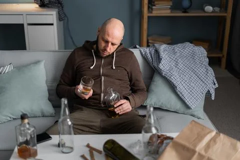 Asleep lonely drunk man on sofa with bottle and glass. The house is mess. Dep Stock Photos
