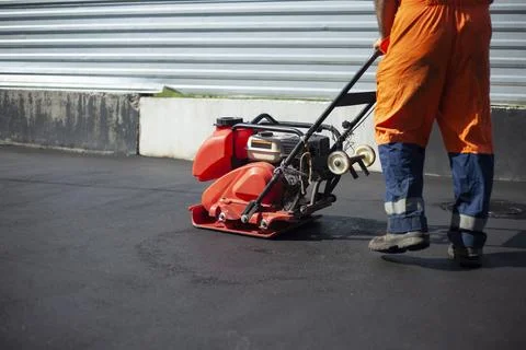 Asphalt paving machine. Worker compacts roadway. Repair of road. Stock Photos