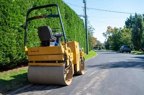 Asphalt paving roller sits empty on a suburban road and no workers Stock Photos