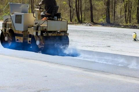 An asphalt roller is used by a worker to lay asphalt on new road Stock Photos