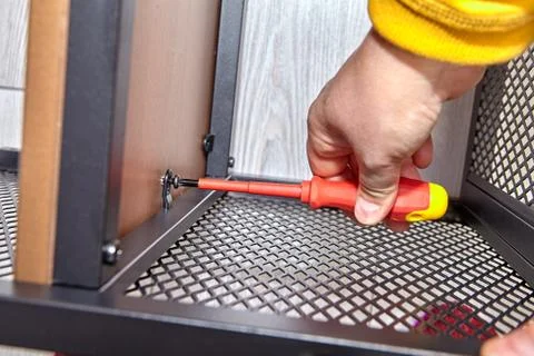 Assembler is mounting metal flat pack furniture using screwdriver. Stock Photos