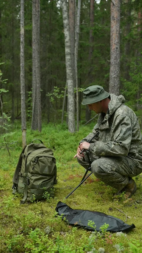 Assembling a black folding camp chair on the mossy ground in a forest Stock Footage 340653502