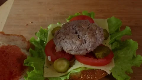 Assembling gourmet burger with meat patty, lettuce, tomato, cheese on woode.. Stock Footage 345061047
